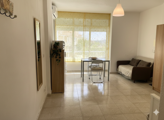 🌟 OPORTUNIDAD DE INVERSIÓN: Estudio Luminoso con Piscina en Calle Isabel Manoja, Torremolinos – con inquilino buen pagador. Sala luminosa con un sofá marrón, mesa y ventanas con cortinas claras.